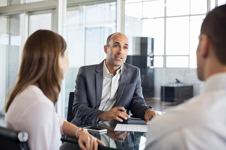 A business professional in a suit having a conversation with a couple during a consultation in a modern office.