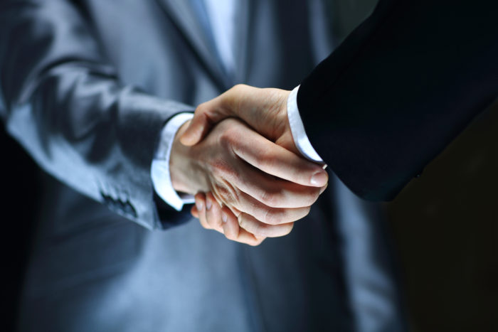 Close-up of two business professionals in suits shaking hands, symbolizing agreement or partnership.