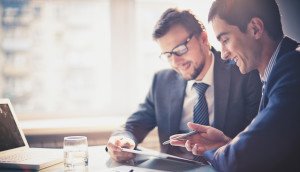 Two businessmen discussing something while looking at a tablet.