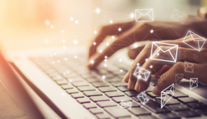 Hands typing on a laptop keyboard with floating email icons, symbolizing digital communication.