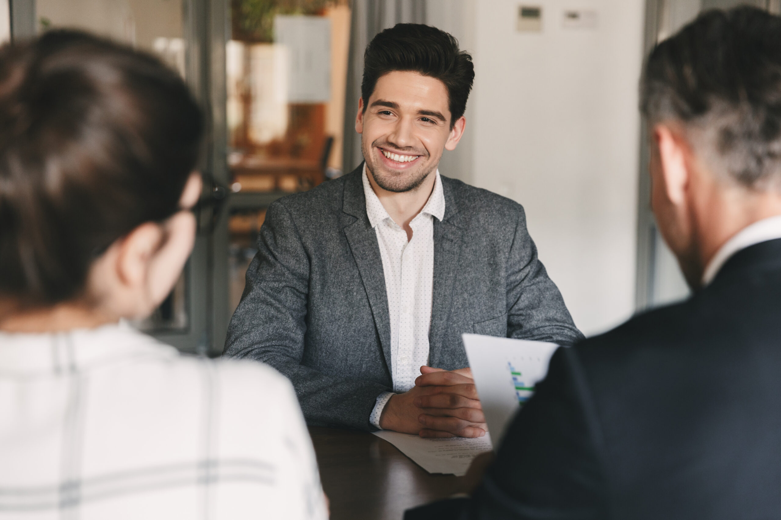 Smiling man in a suit sitting across from colleagues in a meeting room.