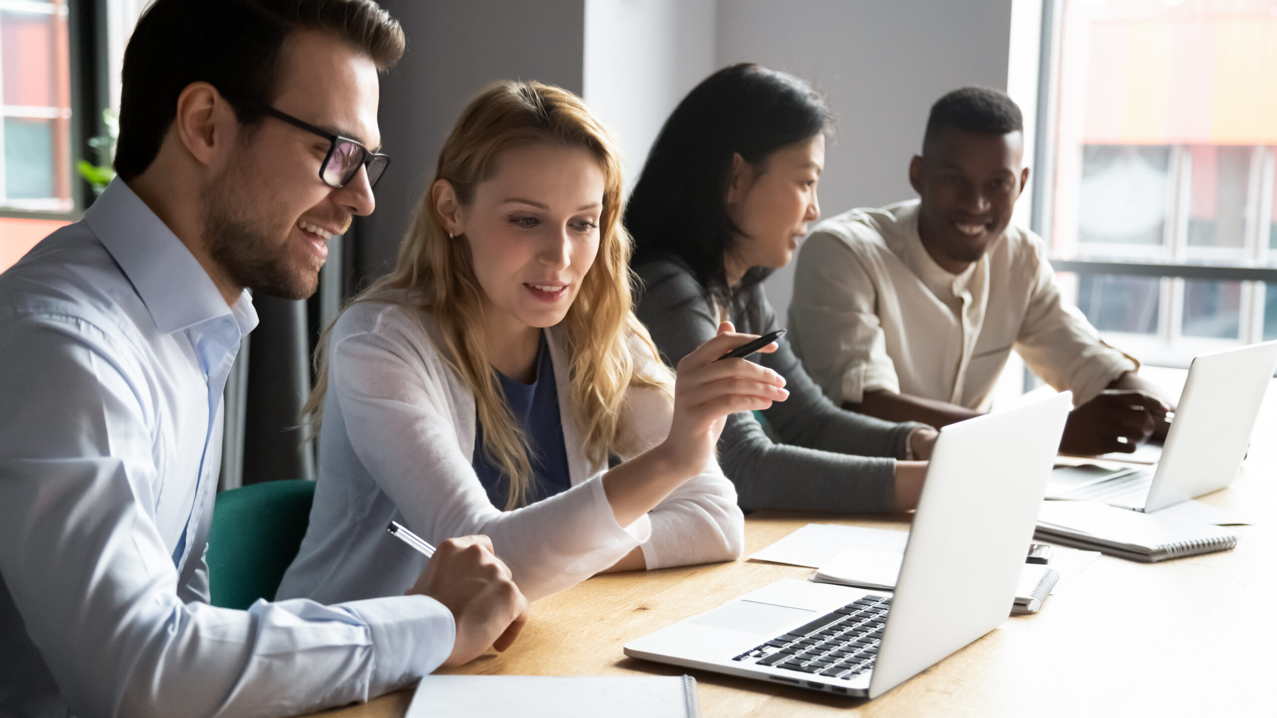 Group of diverse colleagues discussing work while gathered around a laptop.